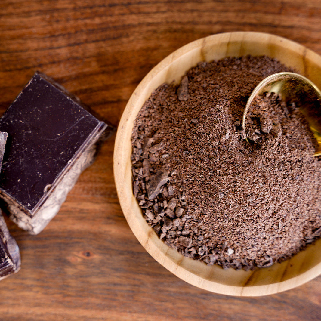 Solid Cacao bars and a wooden bowl with grated cacao on a wooden surface